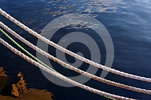 Mooring ropes and blue water sea. White nautical cords