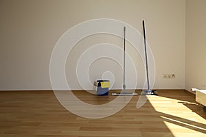 A mop and bucket and a broom stand on a parquet floor in an empty room