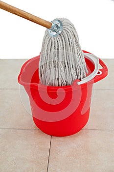 Mop in red bucket on tile floor