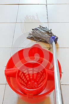 Mopping the tile floor by swab and red bucket