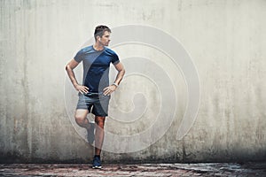 The more challenges you endure, the more you will change. a sporty young man standing against a grey wall while