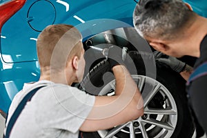 For more smooth wheels. Two male mechanics using torch for inspecting wheel of lifted car at auto repair shop