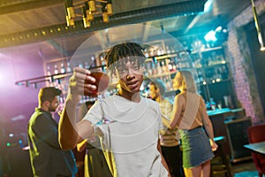 More Vibe, More Fun. Cheerful mixed race young man getting drunk, posing with a cocktail in his hand. Friends
