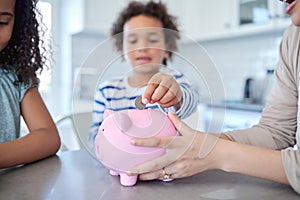 The more you add, the more it grows. an unrecognizable mother teaching her kids about savings at the kitchen table.