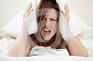 Morning already. Portrait of an angry young woman shouting while lying in bed with a pillow over her head.