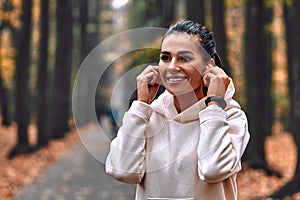 Morning autumn jog. Young beautiful woman adjusts headphones before jogging