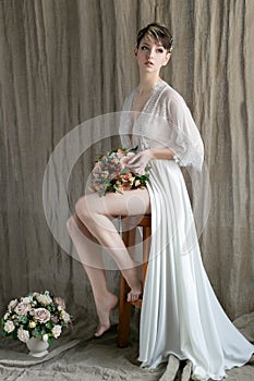 Morning beautiful delicate bride with short hair with a small wreath silk underwear sitting on a chair with a wedding bouquet