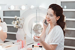 Morning of beautiful young woman applying makeup and talking by phone at home