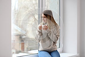 Morning of beautiful young woman drinking hot coffee near window