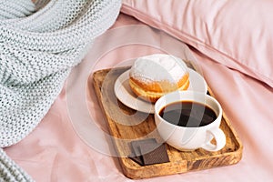 Morning breakfast in bed with fresh and hot bracing coffee, a doughnut in powdered sugar and three slices of chocolate