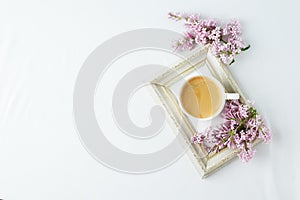 Morning breakfast with coffee cup and lilac branches on white background. Flat lay, top view women background. Minimal concept,