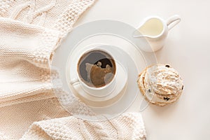 Morning breakfast, a cup of black coffee with milk and pastries in the pastel colors with warm gentle scarf on a white. Top view.