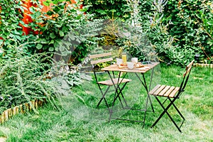 Morning Breakfast In Green Garden With French Croissant, Coffee Cup, Orange Juice, Tablet and Notes Book On Wood Table