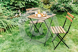 Morning Breakfast In Green Garden With French Croissant, Coffee Cup, Orange Juice, Tablet and Notes Book On Wood Table