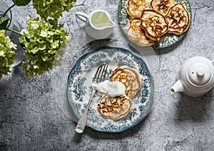 Morning breakfast table - apples pancakes with sour cream, teapot, bouquet of hydrangeas on a gray background, top view