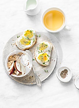 Morning breakfast table inspiration - sandwiches with cream cheese and boiled egg, yogurt with apple and flax seeds, herbal detox