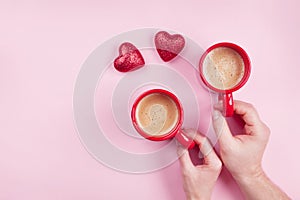 Morning breakfast for Valentines day. Couple holding cups of coffee and red hearts on pink background top view. Flat lay