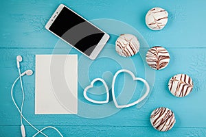 Morning breakfast for Valentines day. Smartphone, chocolate candies, card for text, two decorative hearts on blue background. Top