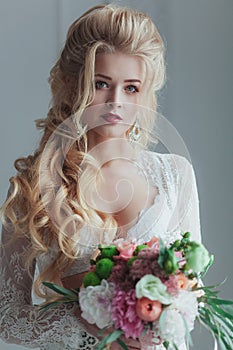 Morning of the bride. Beautiful young woman in white negligee staying near the window with a bouquet