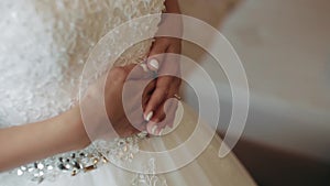 Morning bride. Bridesmaid tying bow on wedding dress. Woman`s hands lace up silk ribbon on bride`s corset. Helping to