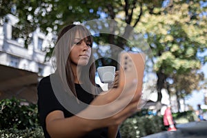 Morning in cafe - attractive woman in black drinkin coffe and make selfie photo for social networks