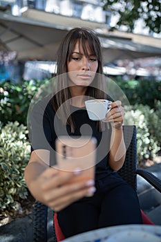 Morning in cafe - attractive woman in black drinkin coffe and make selfie photo for social networks