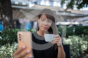 Morning in cafe - attractive woman in black drinkin coffe and make selfie photo for social networks