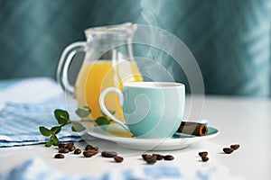 Morning coffee in a blue cup beside cinnamon and scattered coffee beans, in the background a jug with orange juice