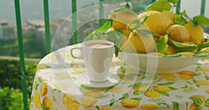 A morning coffee beside a bowl of fresh lemons on a balcony. Serene panoramic view of coastal town that invites