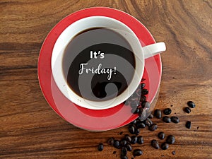 Morning coffee concept with reminder text - It is Friday. On background of a cup of black coffee, raw coffee beans on wooden table