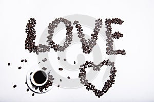 Inscription made of coffee beans on white background next to a cup of coffee