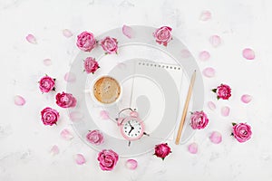 Morning coffee cup for breakfast, empty notebook, petals, alarm clock and pink rose flowers on white table top view flat lay