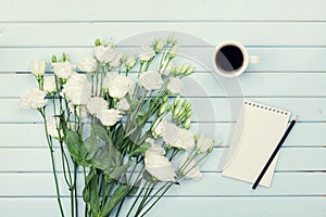 Morning coffee cup, empty paper list, pencil, and bouquet of white flowers eustoma on blue rustic table top view. Flat lay.