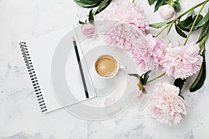 Morning coffee mug for breakfast, empty notebook, pencil and pink peony flowers on white stone table top view in flat lay style.