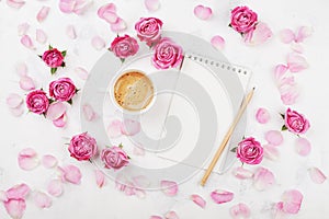 Morning coffee mug for breakfast, empty notebook, petal and pink rose flowers on white table top view in flat lay style.