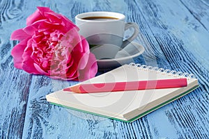 Morning coffee mug, empty notebook, pencil and white peony flowers on blue wooden table
