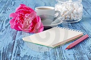 Morning coffee mug, empty notebook, pencil and white peony flowers on blue wooden table