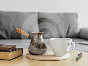 Morning coffee still life in the interior. Coffee cup, cezve and books on table, gray sofa background. Stay home concept