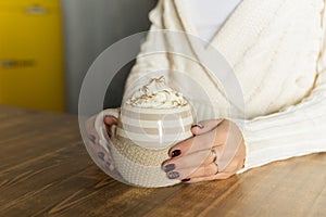 Morning coffee with whipped cream. winter composition. Hand with a cup of Cappuccino or latte coffee on christmas lights