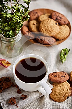 Morning coffee in white cup, chocolate chips cookies on cutting board close-up, selective focus