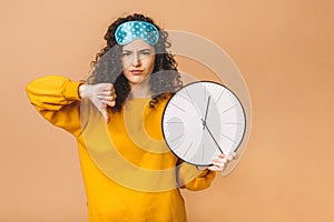 Morning concept. Beautiful curly young woman posing over beige background with clock and sleeping mask