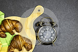 Morning concept - Fresh baked croissants on cutting board for breakfast with alarm showing 7 o` Clock