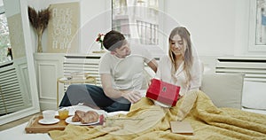 In the morning couple taking breakfast together in bedroom and man surprise his woman and giving a perfect gift.