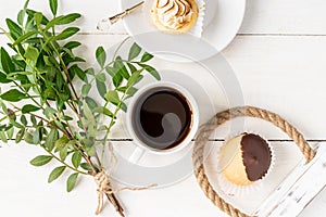 Morning cup of coffe, mini dessert and bunsh of green sprig leaves. Top view, light and airy flat lay