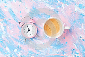 Morning cup of coffee and alarm clock on colorful working desk top view in flat lay style. Punchy pastel background.