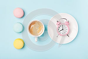 Morning cup of coffee, cake macaron and alarm clock on light turquoise table top view. Flat lay style. Beautiful breakfast.