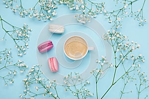 Morning cup of coffee, cake macaron and flower gypsophila on blue table from above. Cozy breakfast. Flat lay style.