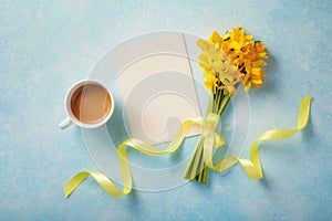 Morning cup of coffee, clean card and spring daffodil flowers on blue background. Beautiful breakfast for Woman day, Mother day.