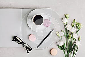 Morning cup of coffee, empty notebook, pencil, glasses, white flowers and cake macaron on light table top view.