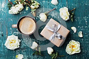 Morning cup of coffee, gift box and beautiful roses flowers on teal vintage table top view. Cozy Breakfast. Flat lay style.